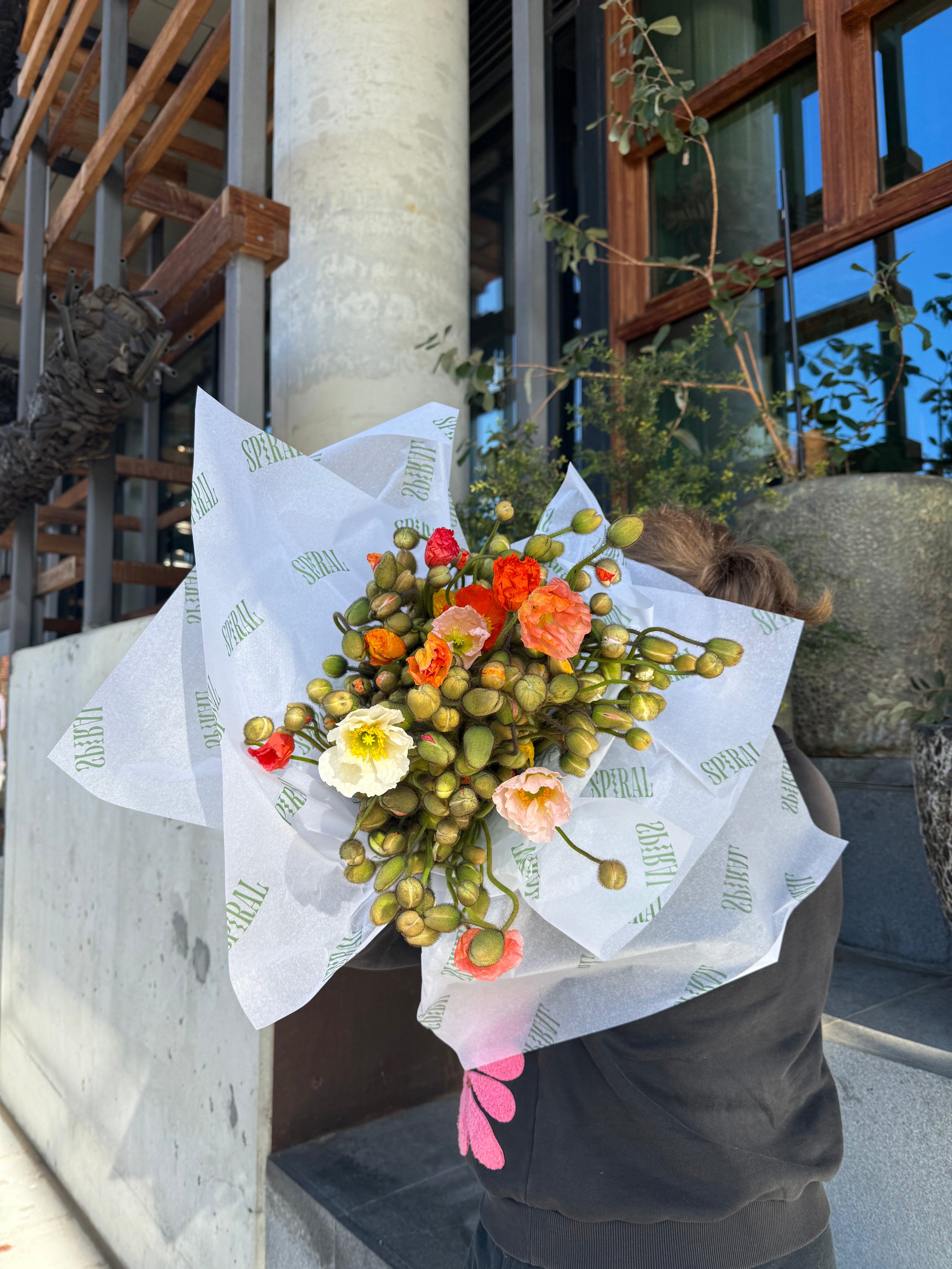 Bouquet of flowers held by a person with a building and window in the background